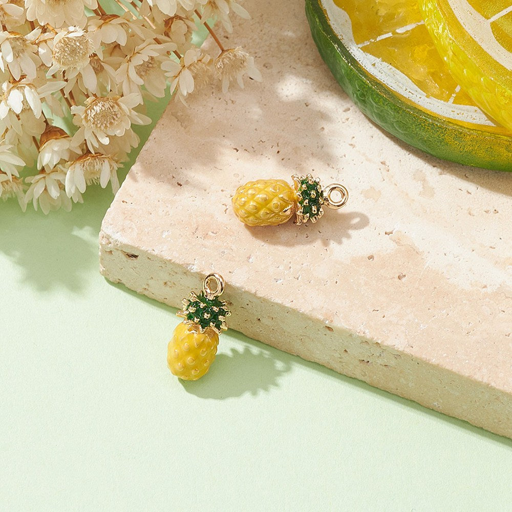 Two yellow enamel pineapple charms with green leaf crown and gold loops on a block