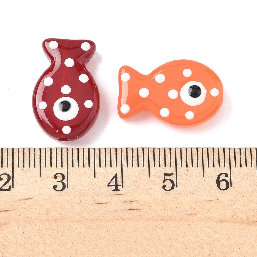 Fish-shaped glass enamel beads on size ruler: red and orange with white dots, black eyes