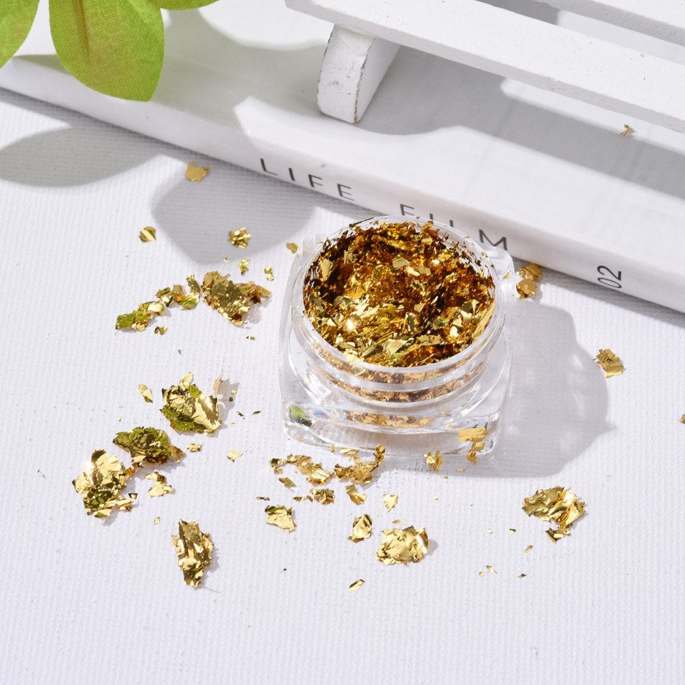 Golden metallic foil flakes in open mini jar with loose flakes around
