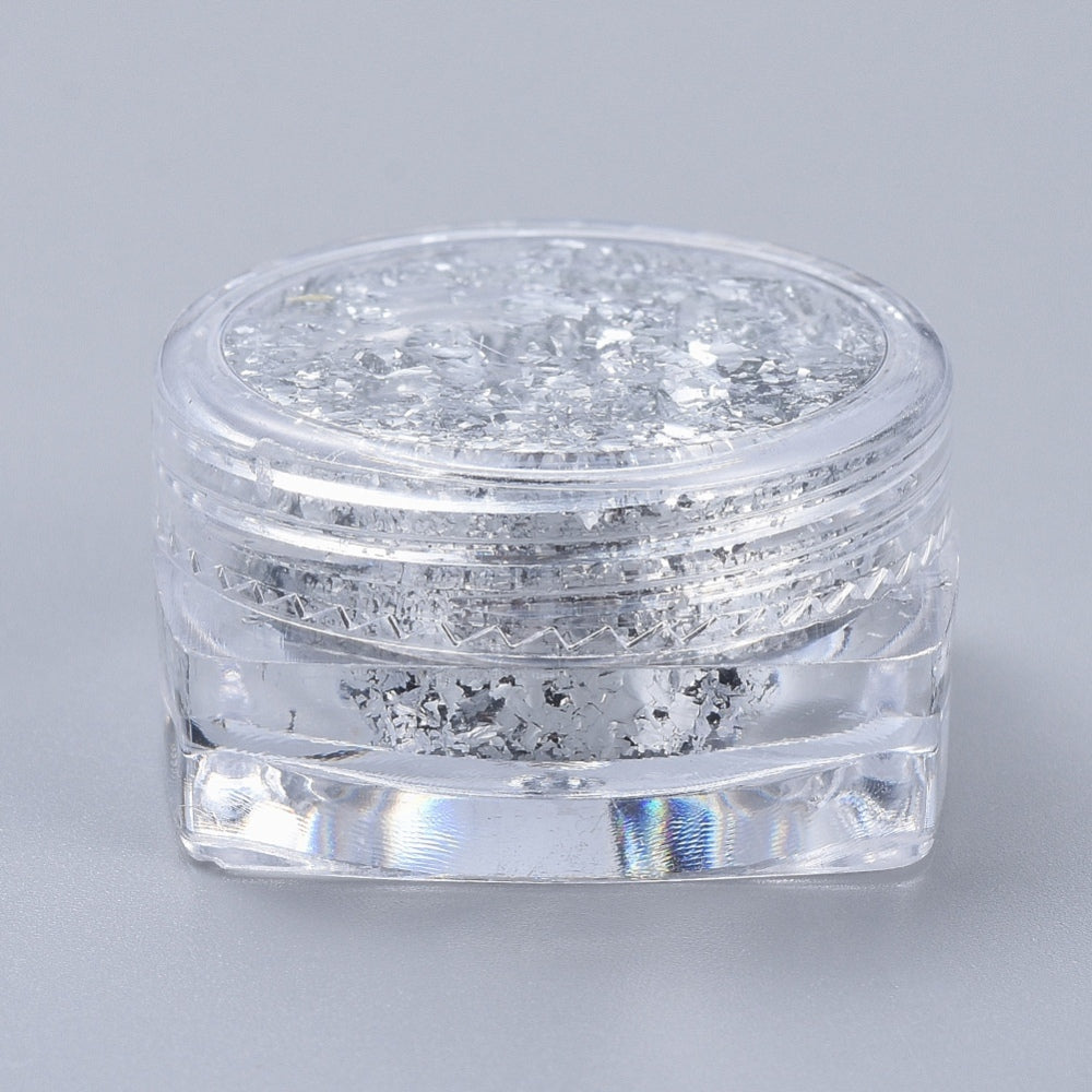 Silver metallic foil flakes in clear small jar with chunky reflective pieces