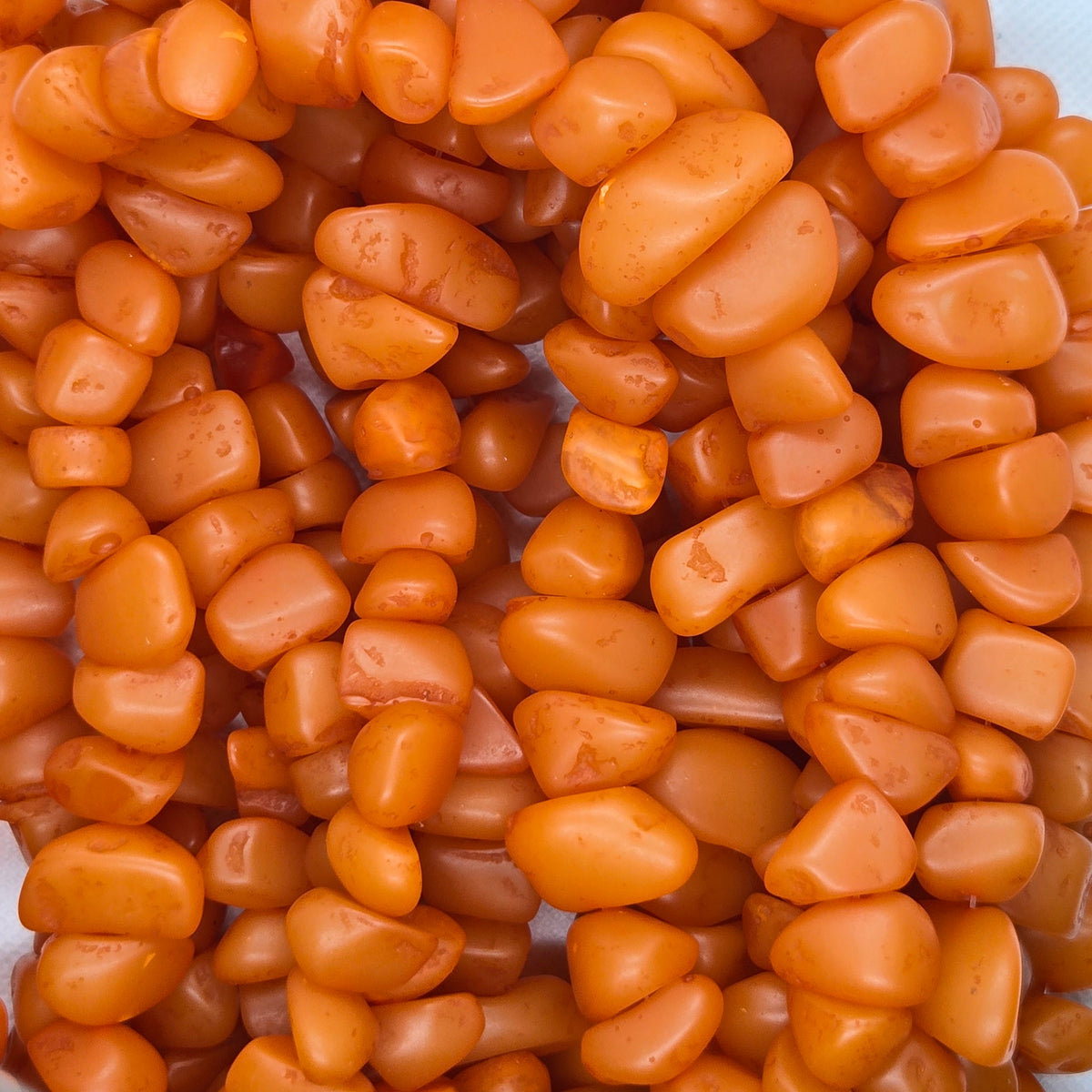 Orange chip resin beads, irregular shapes, close-up on the strand.