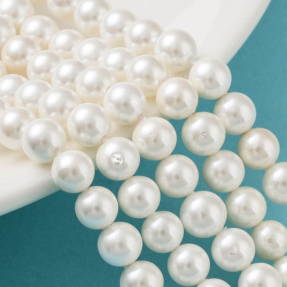 Round white shell pearl beads on a curved strand, close-up on bead surfaces