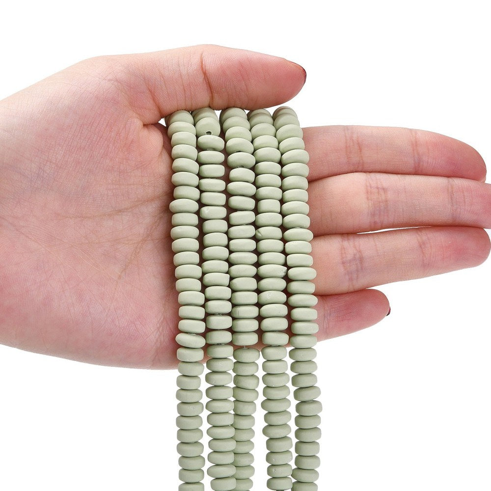 Pale green flat round polymer clay bead strand held in hand, stacked ridged discs