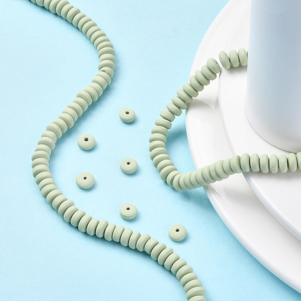 Pale green flat round polymer clay beads strand with loose beads scattered