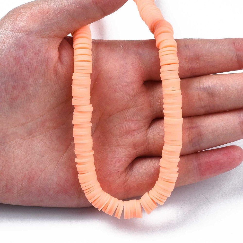 Light salmon heishi disc beads strand held in hand; round discs with center holes