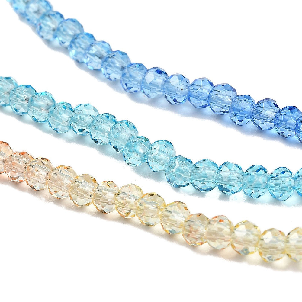 Transparent faceted glass rondelle beads close-up: aqua, light blue, and creamy peach strands.