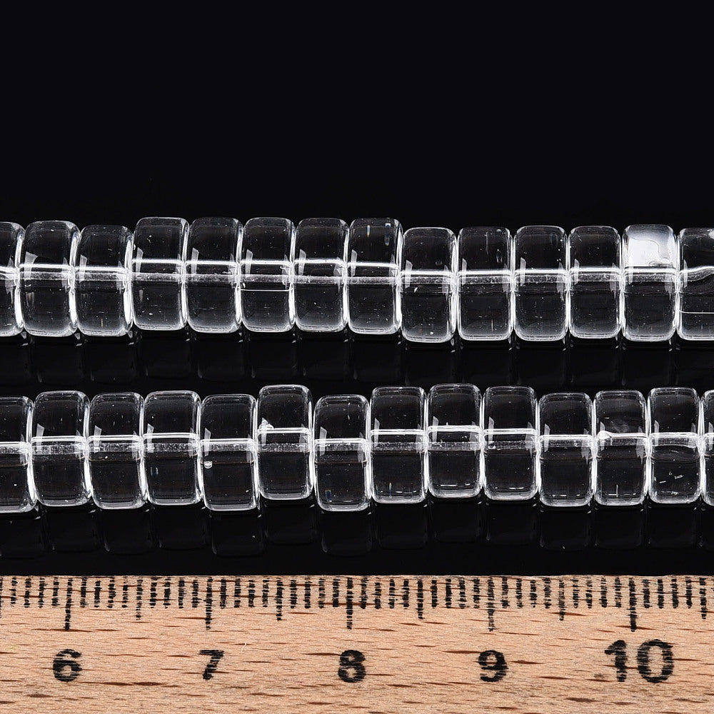 Clear flat round glass bead strand laid across a ruler, square holes