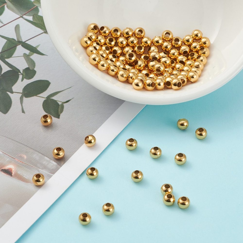 Set of round gold-plated beads with threading holes, scattered on a surface