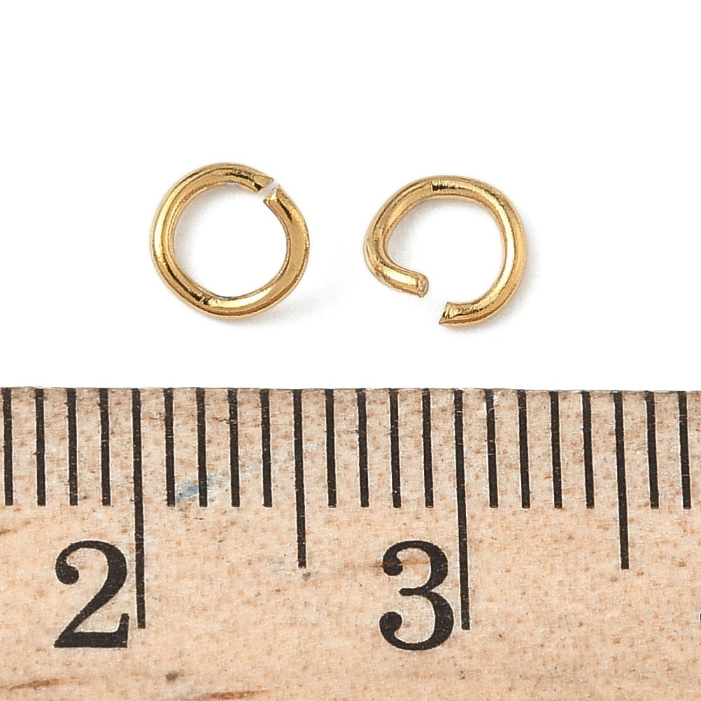 Gold-plated open jump rings beside ruler markings for scale