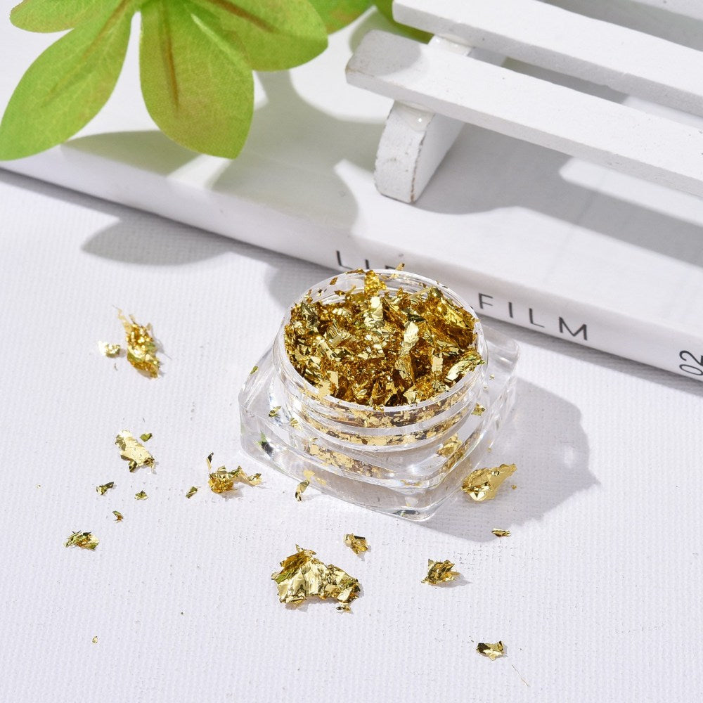 Gold metallic foil flakes scattered near a small open clear storage jar